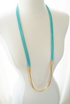 a white mannequin with a blue and gold necklace on it