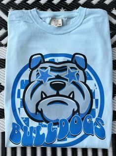 Get this popular new Bulldogs Mascot shirt and show off your school spirit in style!  Each shirt is printed in-house by me using high-quality materials on a Comfort Colors shirt, known for its exceptional comfort, style, and durability. Shown in Chambray. Even the glitter is printed! No need to worry about peeling glitter vinyl, or messy glitter flakes. Available in unisex sizes S to 3X, and youth sizes, we've got you covered regardless of your preferred fit. The Preppy Bulldogs Shirt features a Blue Sublimation Design Shirt With Graphic Print For Fans, Blue Graphic Print Sublimation Fan Gear, Blue Graphic Print Sublimation Design For Fan Gear, Blue School Spirit Sublimation T-shirt With Graphic Print, Blue Graphic Print Sublimation Design For School Spirit, Blue School Spirit T-shirt With Heat Transfer Vinyl, Blue School Spirit T-shirt With Sublimation Print, Blue T-shirt With Sublimation Print For School Spirit, School Spirit Graphic Print Shirt For Streetwear