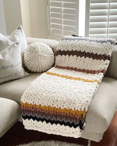 a crocheted blanket sitting on top of a couch next to two throw pillows