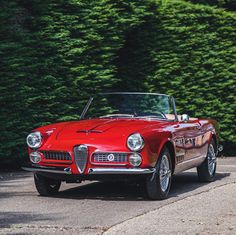 an old red convertible car parked in front of some trees