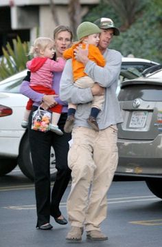 a man walking down the street with two women and a baby in his arms,