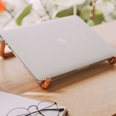 an apple laptop sitting on top of a wooden desk next to glasses and a pen