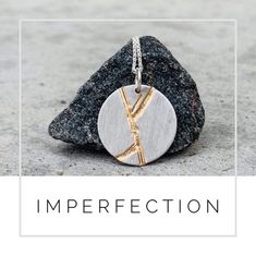 a silver and gold necklace with the word imperfectection on it, sitting next to a rock