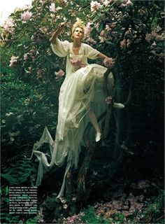 a woman in a white dress sitting on a tree branch with pink flowers around her