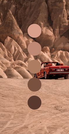 an old red car parked in the desert with circles on it's side and mountains in the background