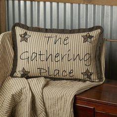 the gathering place pillow sitting on top of a wooden table next to a bed with a striped blanket