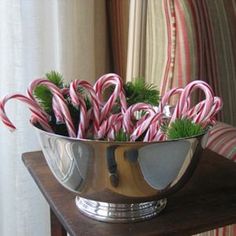 a metal bowl filled with candy canes on top of a wooden table next to a window