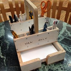 a wooden desk organizer with pens, pencils and scissors in it sitting on a table