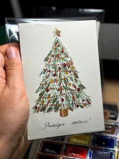 a person holding up a card with a watercolor christmas tree on the front and bottom