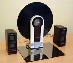 a record player and speakers are sitting on a glass table with a black disc in the center