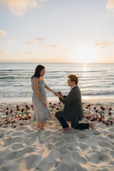 a man kneeling down next to a woman on top of a sandy beach