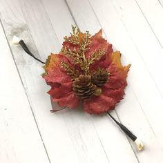 a red and orange flower with pine cones on it's headband, sitting on a white wooden surface