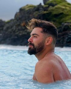 a man in the water with his hair blowing back and looking off into the distance