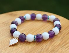 Handcrafted White Jade and Amethyst Beaded Bracelet with Jewel Charm Show your love for Rarity and My Little Pony with this handmade bracelet themed around her! Inspired by her white and purple color scheme and her diamond gem cutie mark, this bracelet is a great way to add a little bit of pony flare to any outfit. It would make a great gift for any fan! The bracelet is made from 8mm genuine white jade and amethyst with an enamel jewel charm. It is strung on elastic cord sized to fit a 6in wrist White Amethyst Beaded Bracelets, White Amethyst Beaded Bracelets As Gift, White Amethyst Beaded Bracelets For Spiritual Style, Handmade White Amethyst Bracelets, White Amethyst Beaded Bracelet As Gift, White Amethyst Spiritual Beaded Bracelets, White Amethyst Round Bead Bracelets, White Amethyst Bracelets With Round Beads, Amethyst Beaded Bracelet