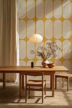 a wooden table with two chairs and a vase on it in front of a yellow patterned wall