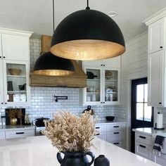 a large kitchen with white cabinets and black pendant lights over the island countertop, along with two vases filled with dried flowers