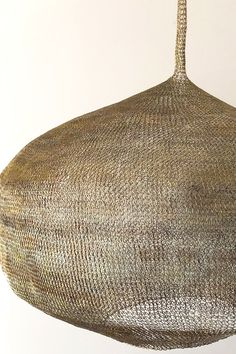 a large woven object hanging from a rope on a wall in front of a white background