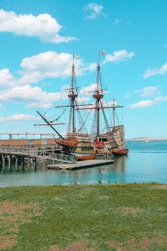 an old sailing ship docked at a pier on the water with grass in front of it