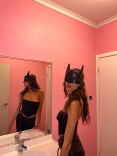 a woman wearing a cat mask standing in front of a bathroom mirror