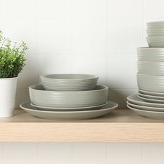 plates and bowls are stacked on a shelf next to a pot with a plant in it