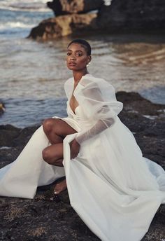 a woman in a white dress sitting on rocks near the ocean