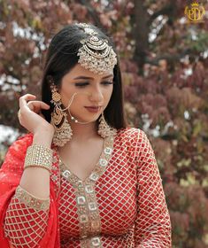 a woman in a red and gold outfit is holding her hands to her ear while looking down