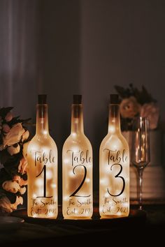 three wine bottles with lights in them on a table