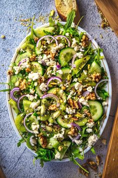 a salad with cucumber, feta cheese and walnuts in a white bowl