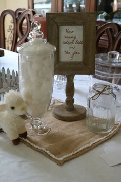 a table topped with a glass vase filled with marshmallows next to a small sheep figurine