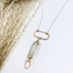 An archway of silver is textured by hand and surrounds a barrel of rutilated quartz, dropping from a gold oval pendant. Beams of gold pass through this unique gemstone accenting the tiny gold link dropping from it. •Sterling Silver and 14k Gold Filled •Rutilated Quartz •Pendant Dimensions: 1.75 x 3/4" •Length: 17" Elegant Silver Mixed Metal Jewelry, Delicate Hammered Sterling Silver Jewelry, Hammered Yellow Gold Oval Link Jewelry, Yellow Gold Hammered Oval Link Jewelry, Silver Hammered Fine Jewelry, Oval Pendant Jewelry With Natural Inclusions In Silver, Hand Forged Gold Oval Jewelry, Delicate Hammered Teardrop Jewelry, Elegant Sterling Silver Jewelry With Natural Inclusions