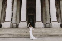 a woman in a white dress standing on some steps with her arms up and flowers in her hair