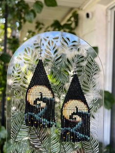 a pair of beaded earrings hanging from a glass frame with leaves on the outside