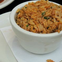 a white bowl filled with rice on top of a table next to plates and utensils