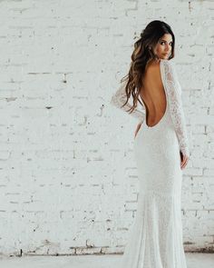 a woman in a white wedding dress standing against a brick wall with her back to the camera