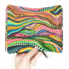 a hand holding a pencil case with an artistic design on the front and back side