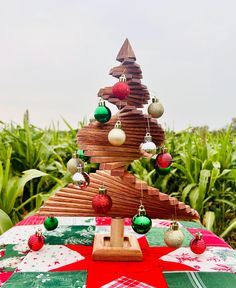 a wooden christmas tree on top of a red and green table cloth with ornaments hanging from it