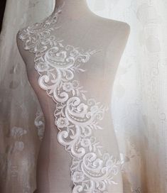 a mannequin with white lace on it's neck and back, in front of a curtain