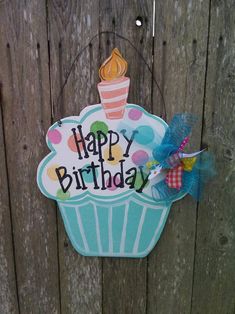 a happy birthday sign hanging on the side of a wooden fence with a cupcake