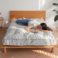 a woman laying on top of a bed next to a wooden headboard and night stand