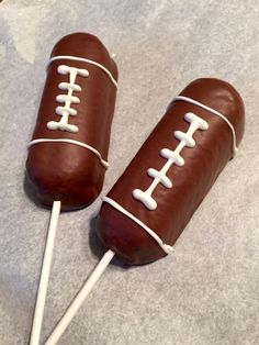 two football shaped chocolate lollipops are on a gray surface with white sticks