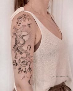 a woman with a bird and flowers tattoo on her arm, standing in front of a white wall