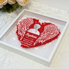 a heart - shaped card with an angel's wings on it and a bouquet of roses in the background