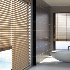 a bath room with a large white tub and window coverings on the windowsill