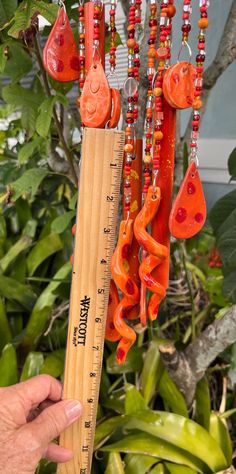 a person holding a wooden ruler in front of a tree filled with orange and red beads