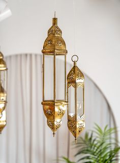 three golden hanging lanterns in the middle of a room with a potted plant next to it