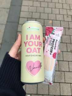 a person holding up a pink and white drink next to a pack of candy bar