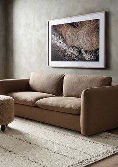 a living room with a couch, ottoman and rug in front of a painting on the wall