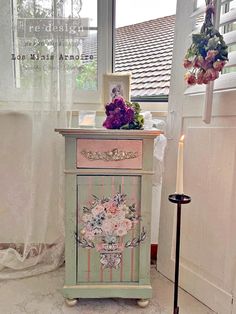 a small cabinet with flowers on it next to a window