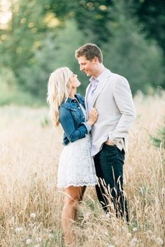 a man and woman are standing in tall grass looking into each other's eyes