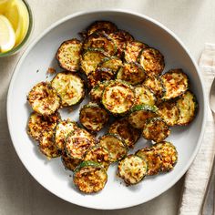 a white bowl filled with cooked zucchini on top of a table next to lemon wedges